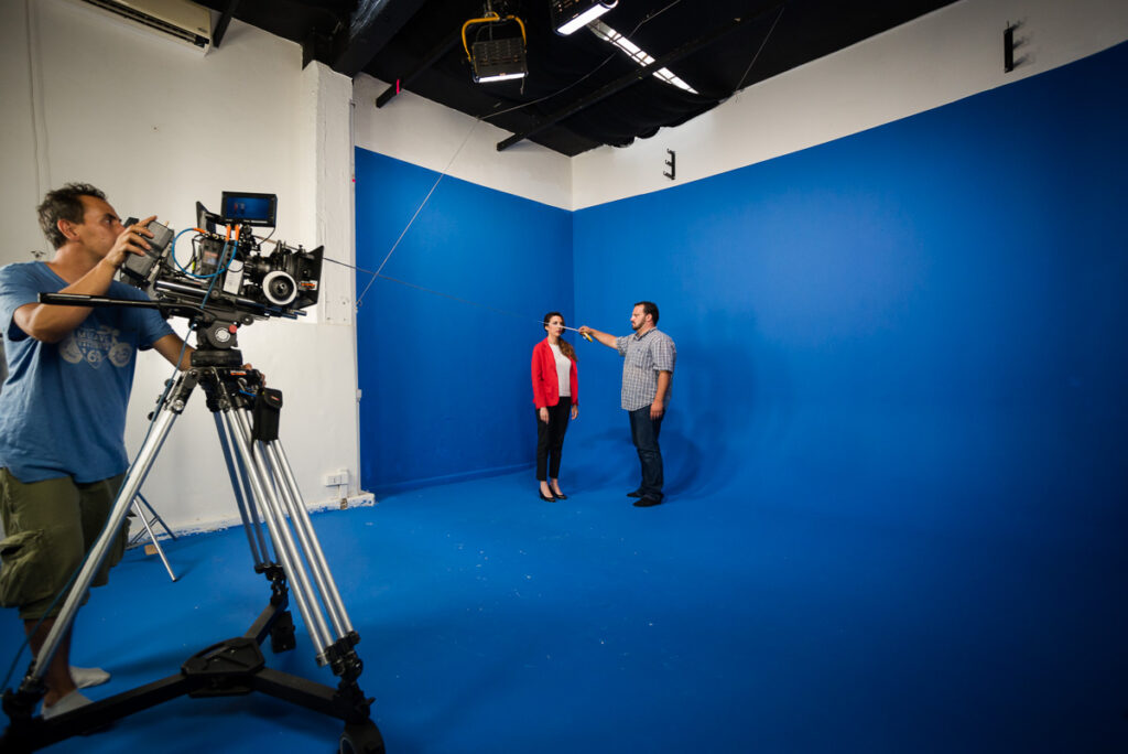 Instudio.org: Model in Red Jacket Shot on Studio C Blue Screen with Camera Operator Measuring Distances for Scene Focus
