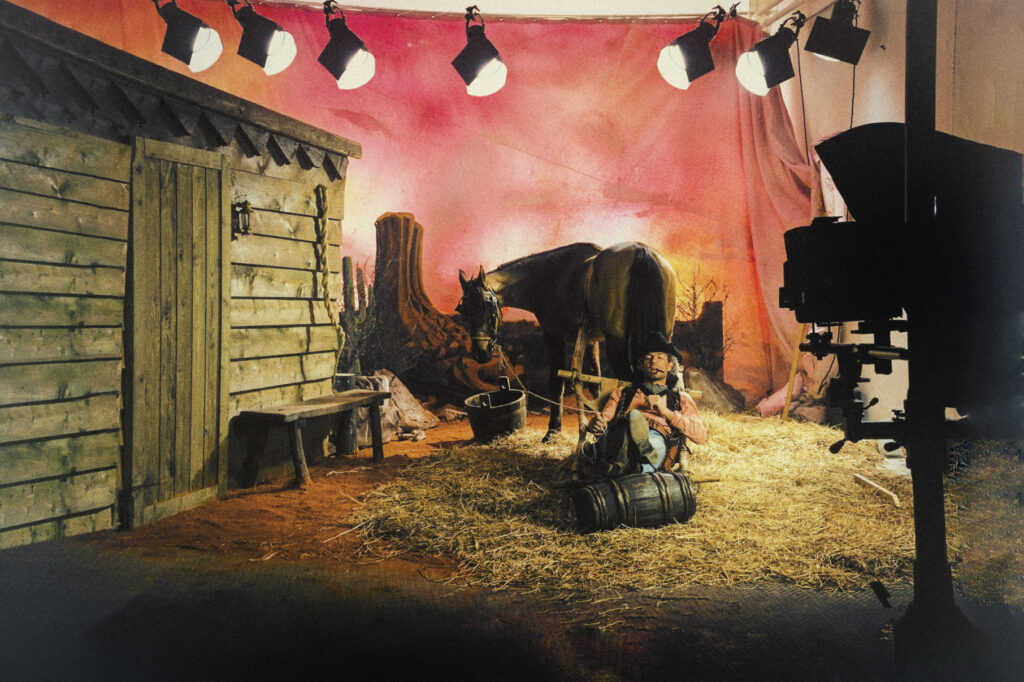 A cowboy and his horse rest in the scenery of Instudio.org a backdrop of a western town.